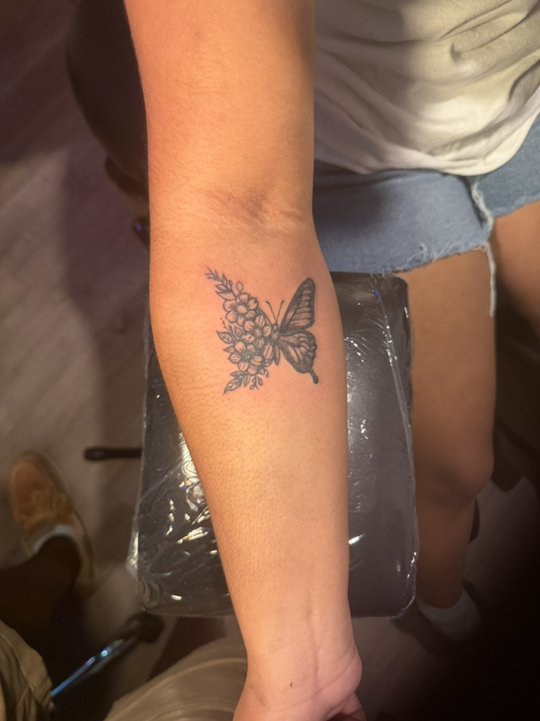Fine-line blackwork butterfly and floral tattoo on forearm