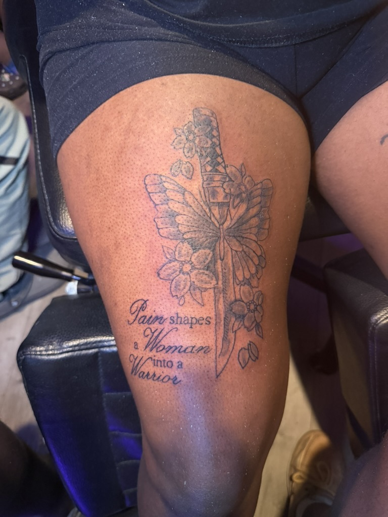 Neo traditional upper-arm tattoo with dagger, butterfly, flowers, and script